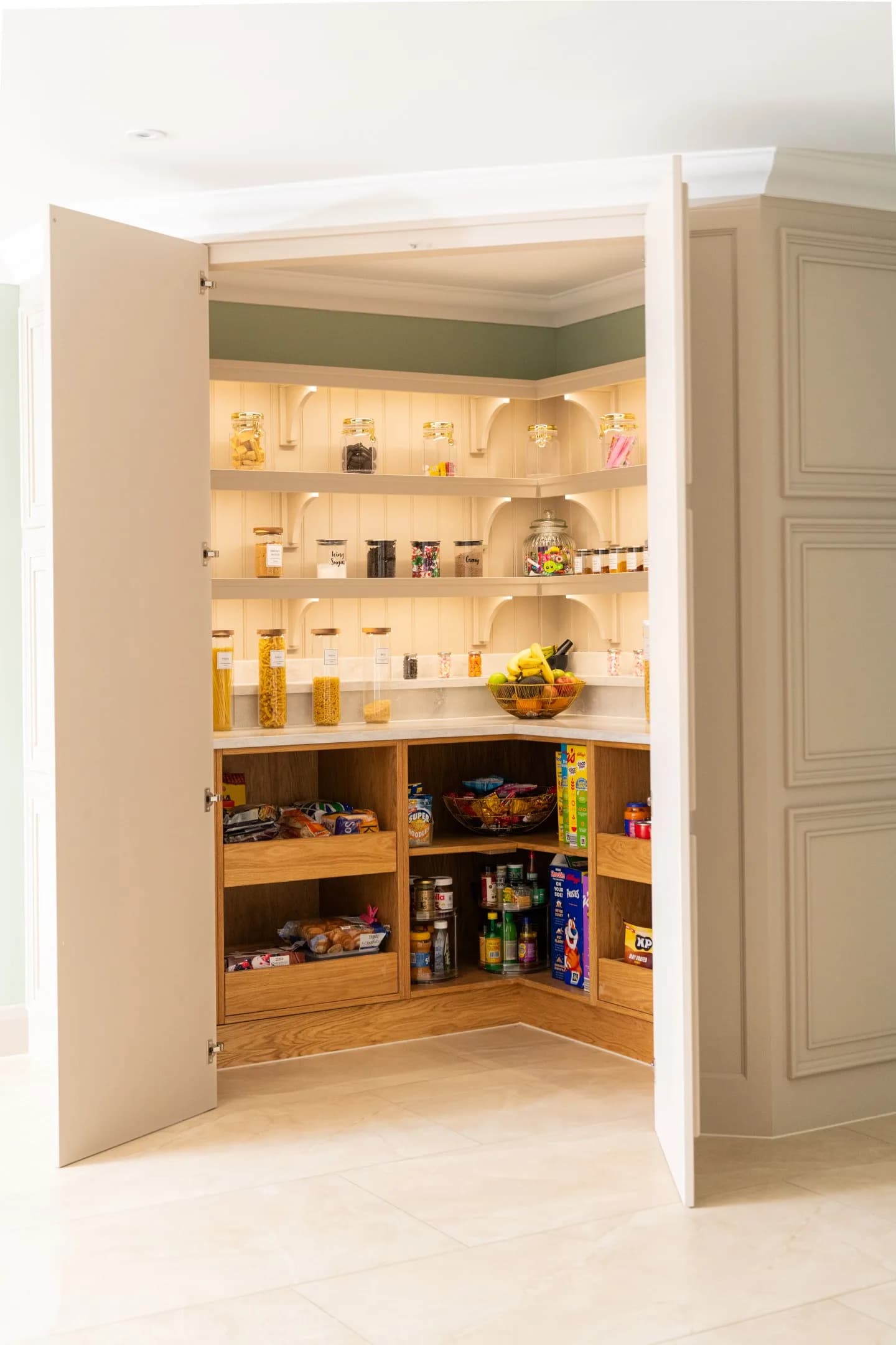 Walk-in corner pantry with its doors open onto lit shelving and oak drawers